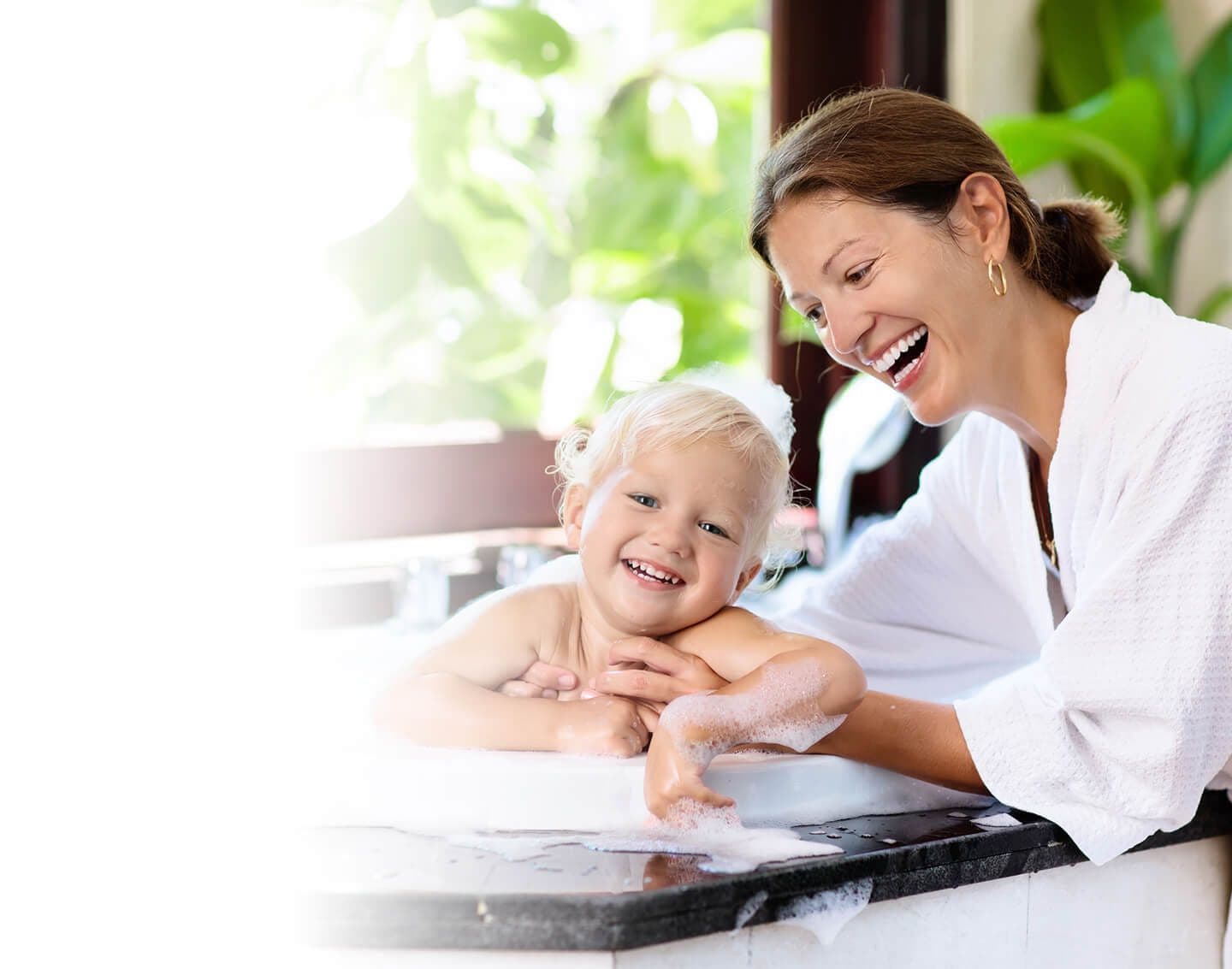 An adult bathes a child in a bath with bubbles.